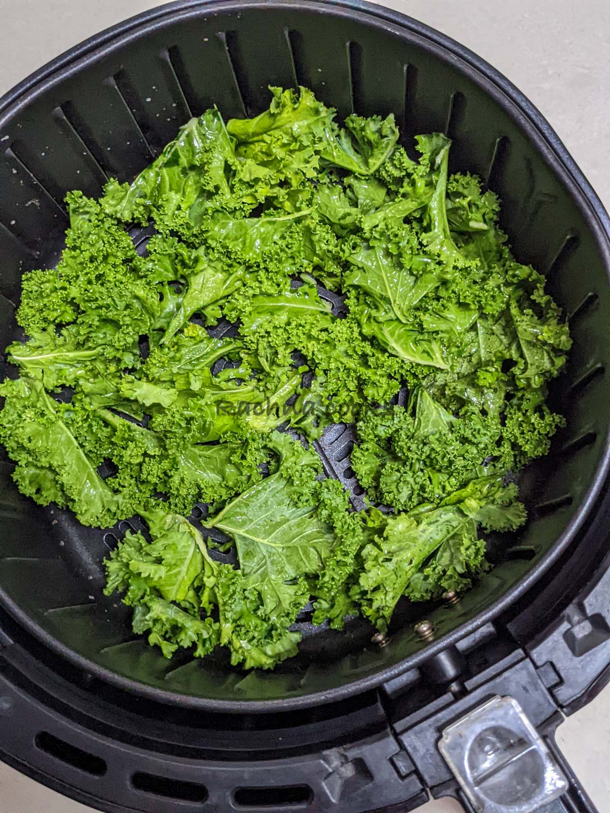Kale leaves kept for air frying in air fryer basket.