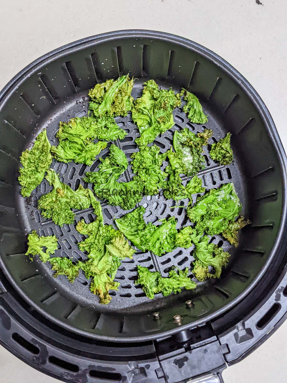 Kale chips done after air frying in air fryer basket.