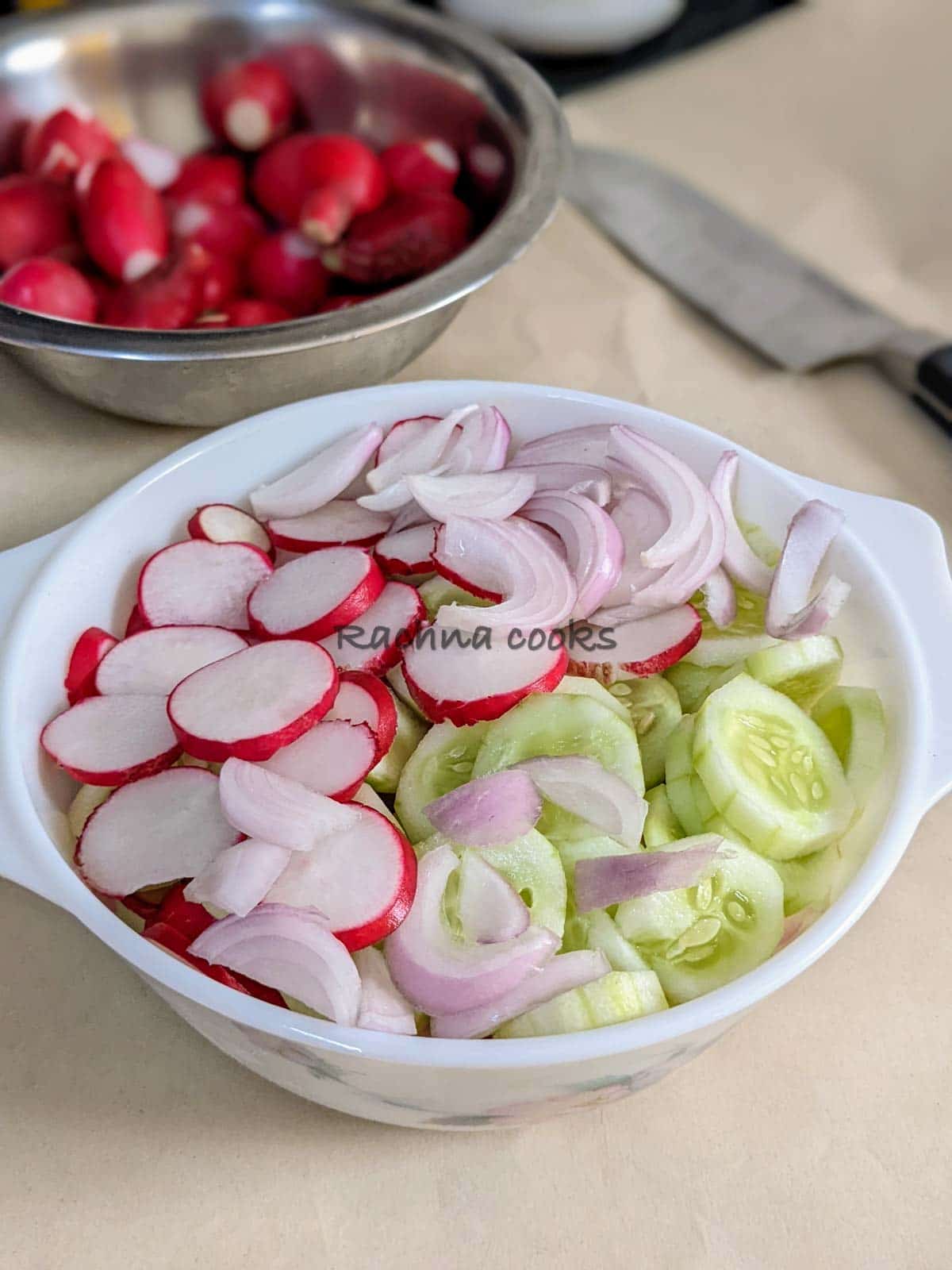 sliced radish, cucumber and onion in a white bowl with radishes in the background.