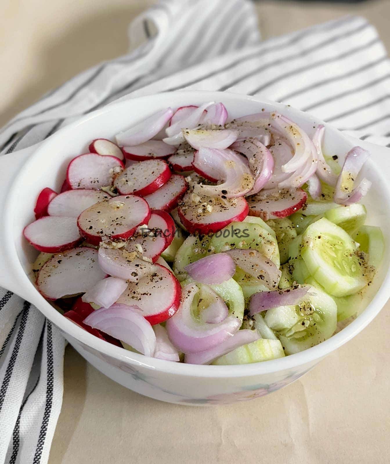Delicious sliced radish, cucumber and onion salad with dressing in a white bowl.