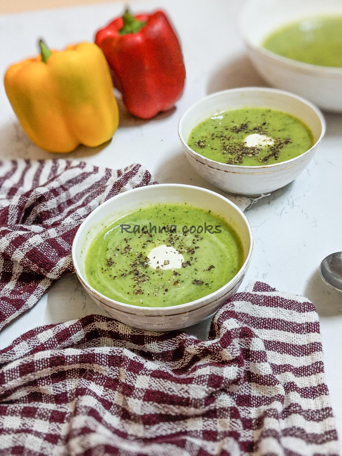 Delicious green zucchini soup in bowls with a dollop of cream and garnished with pepper. Peppers in the background.