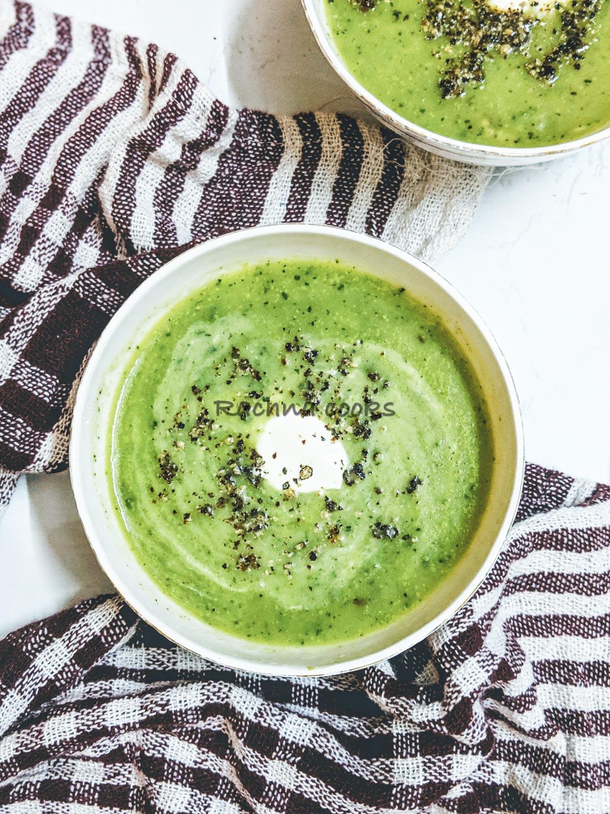 Delicious green zucchini soup bowls with a dollop of cream and garnished with pepper.