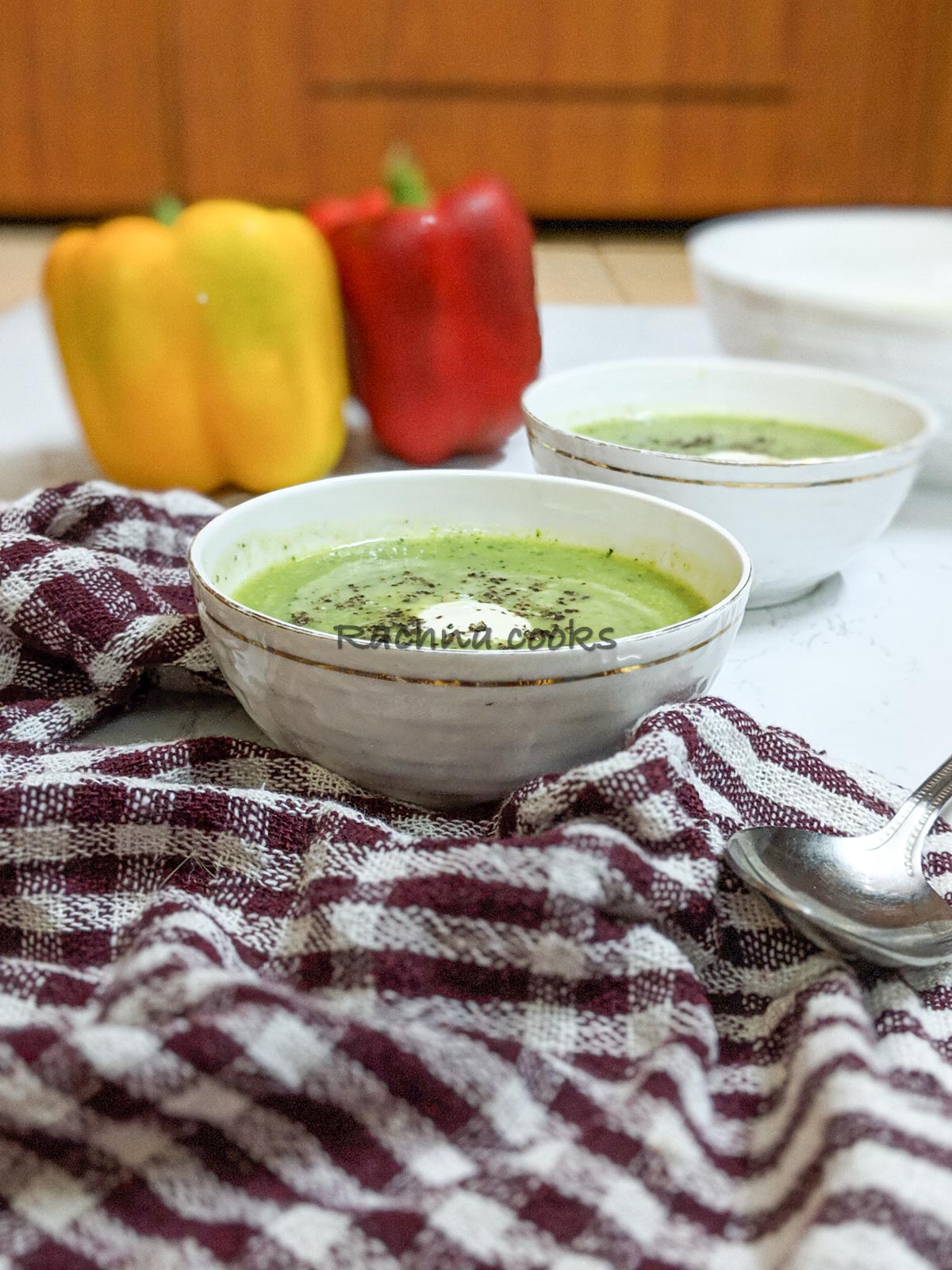 Delicious green zucchini soup in bowls with a dollop of cream and garnished with pepper. Peppers in the background.