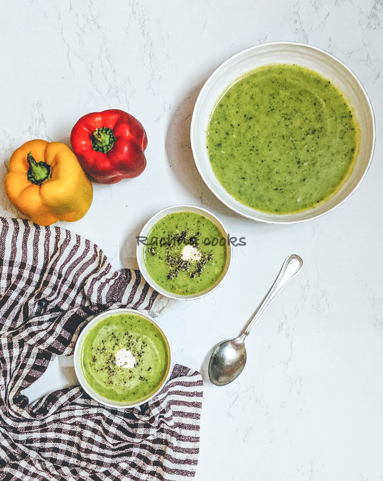 Delicious green zucchini soup in bowls with a dollop of cream and garnished with pepper. Peppers in the background.