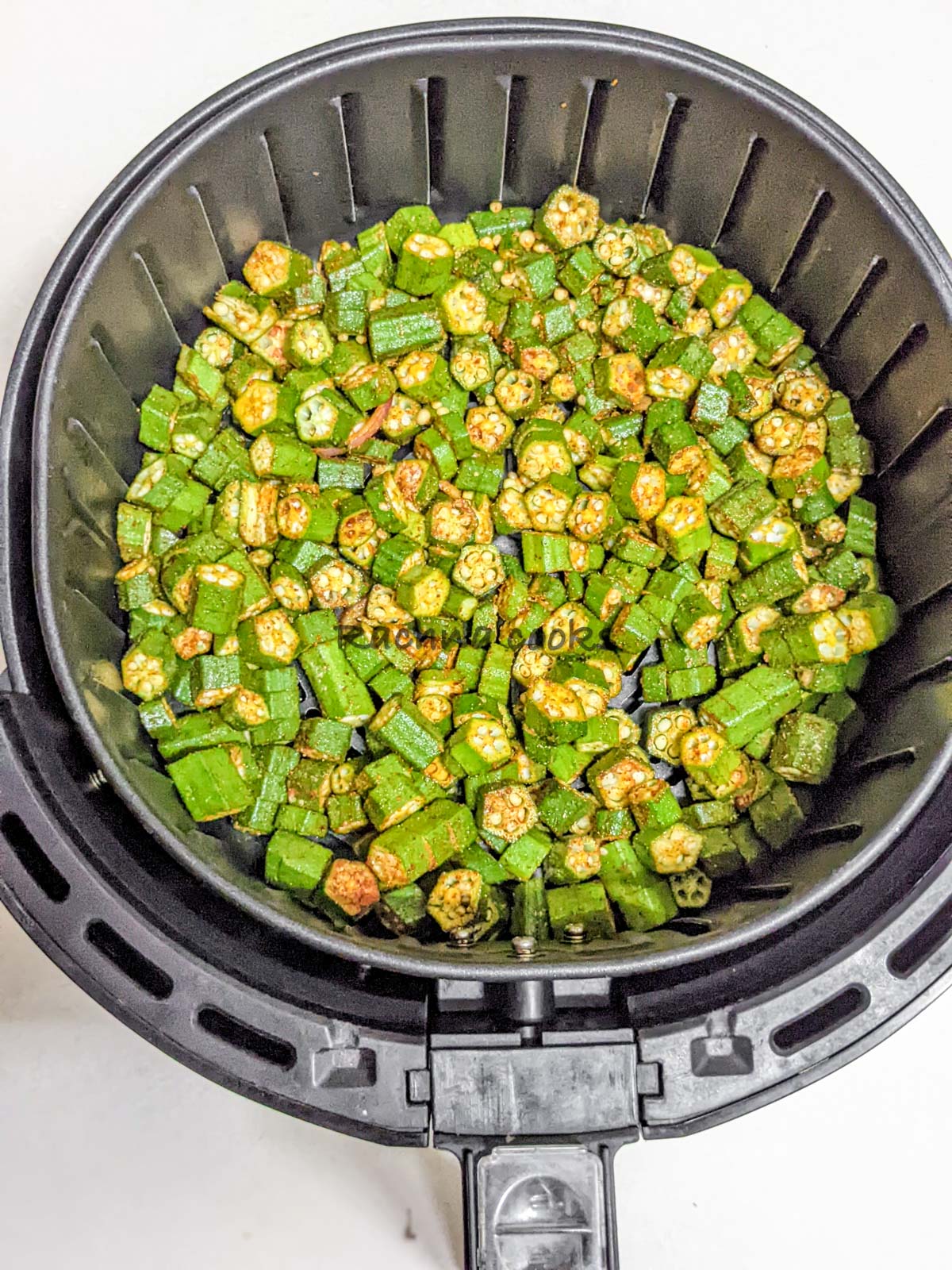 Spiced okra laid in air fryer basket ready for air frying.