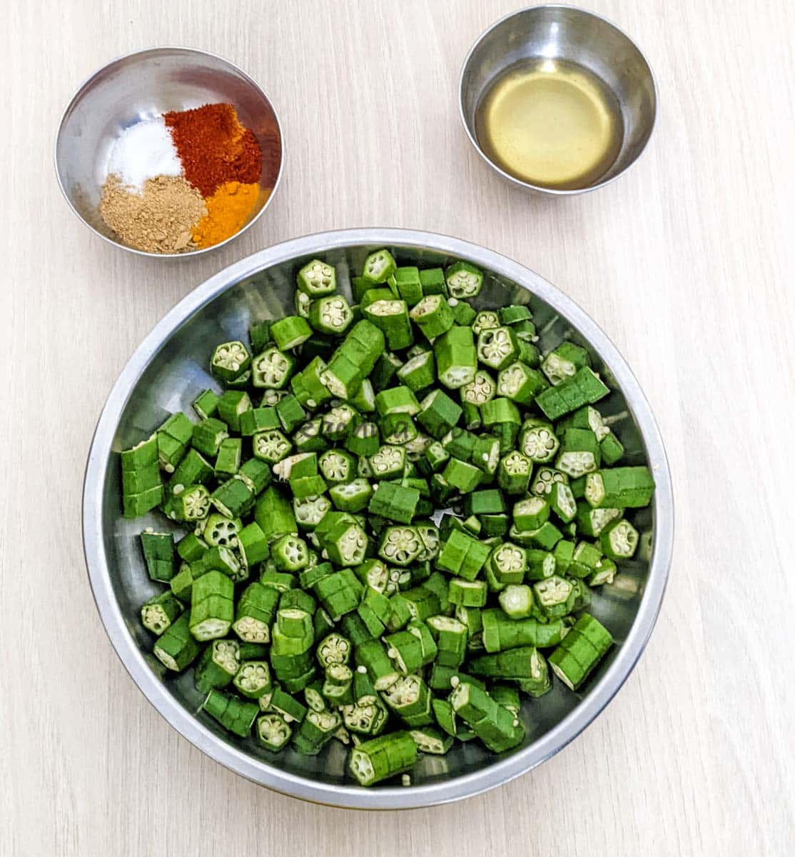 Chopped okra in a shallow plate, bowls of olive oil and spices.