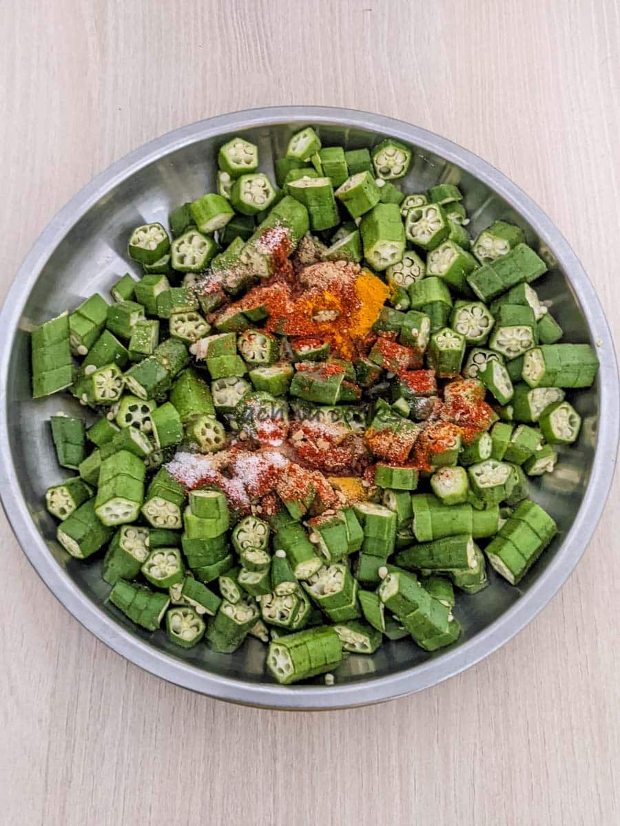 Chopped okra in a shallow plate with spices and oil.