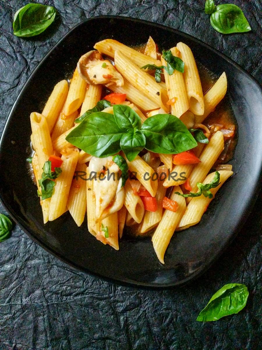 Pasta in red sauce garnished with basil leaves in a black plate.