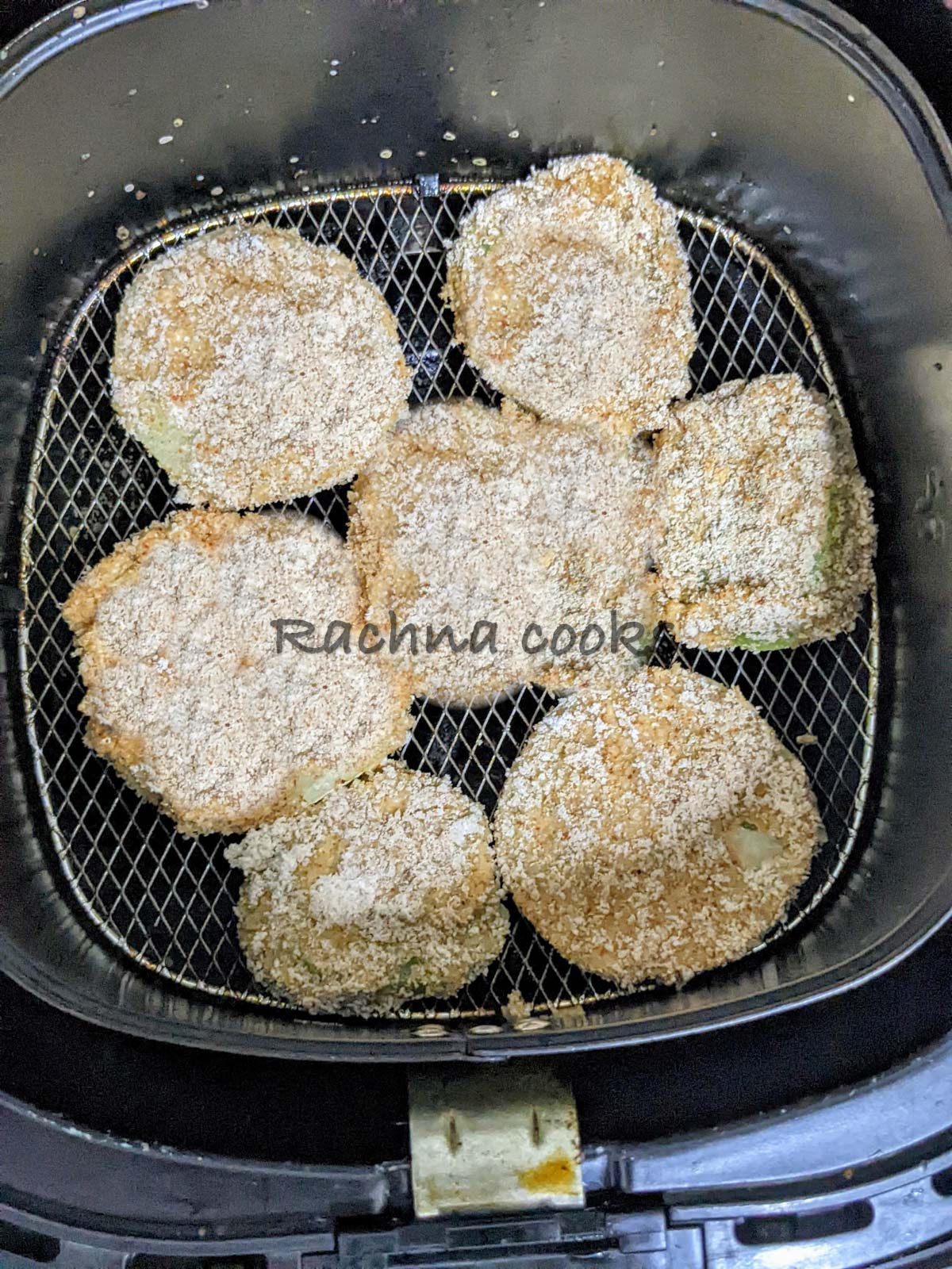 Breaded green tomato slices in air fryer basket.