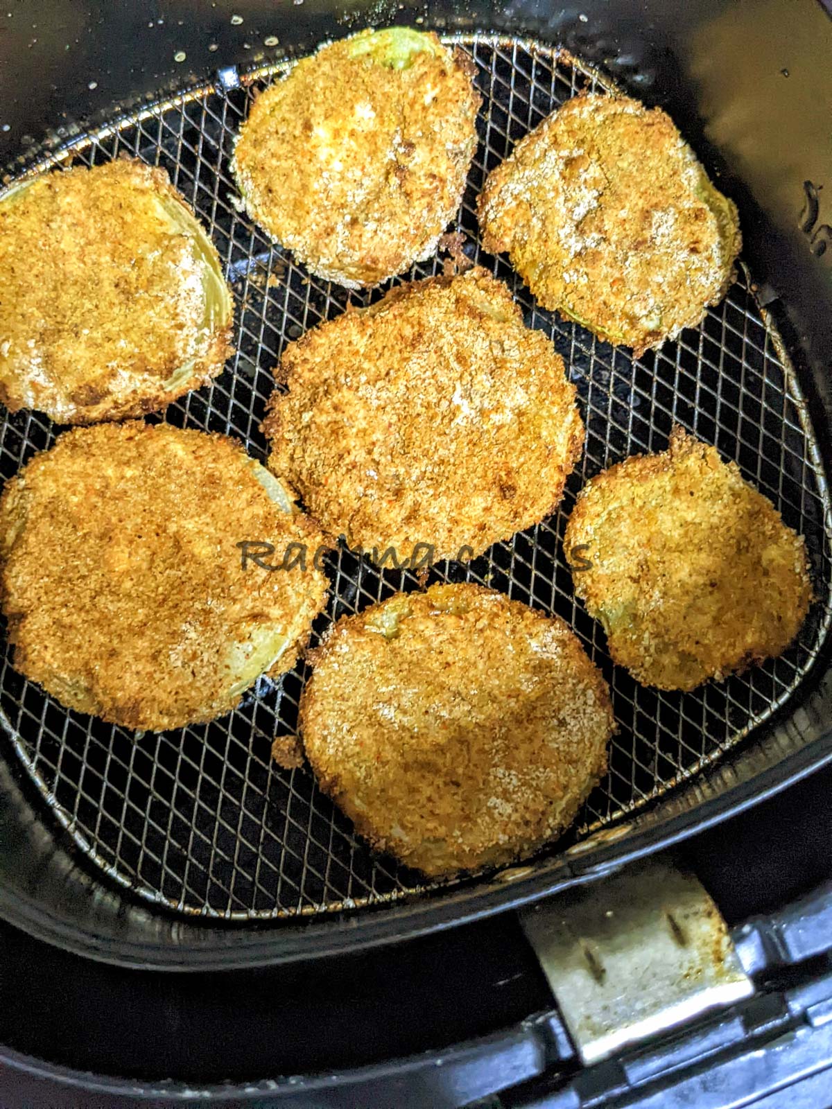 Browned and air fried green tomatoes in air fryer basket.
