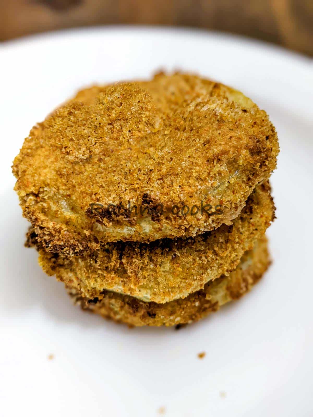 Three air fried green tomatoes piled on top of each other on a white plate.