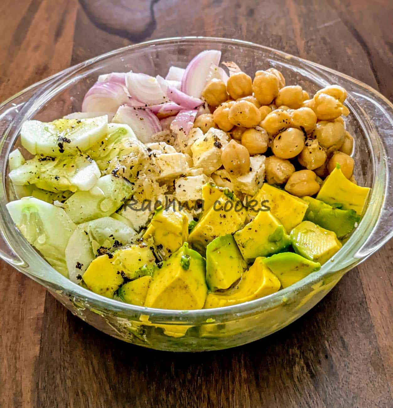 Dressing drizzled over chopped avocado, onion, cucumber, chickpeas and feta