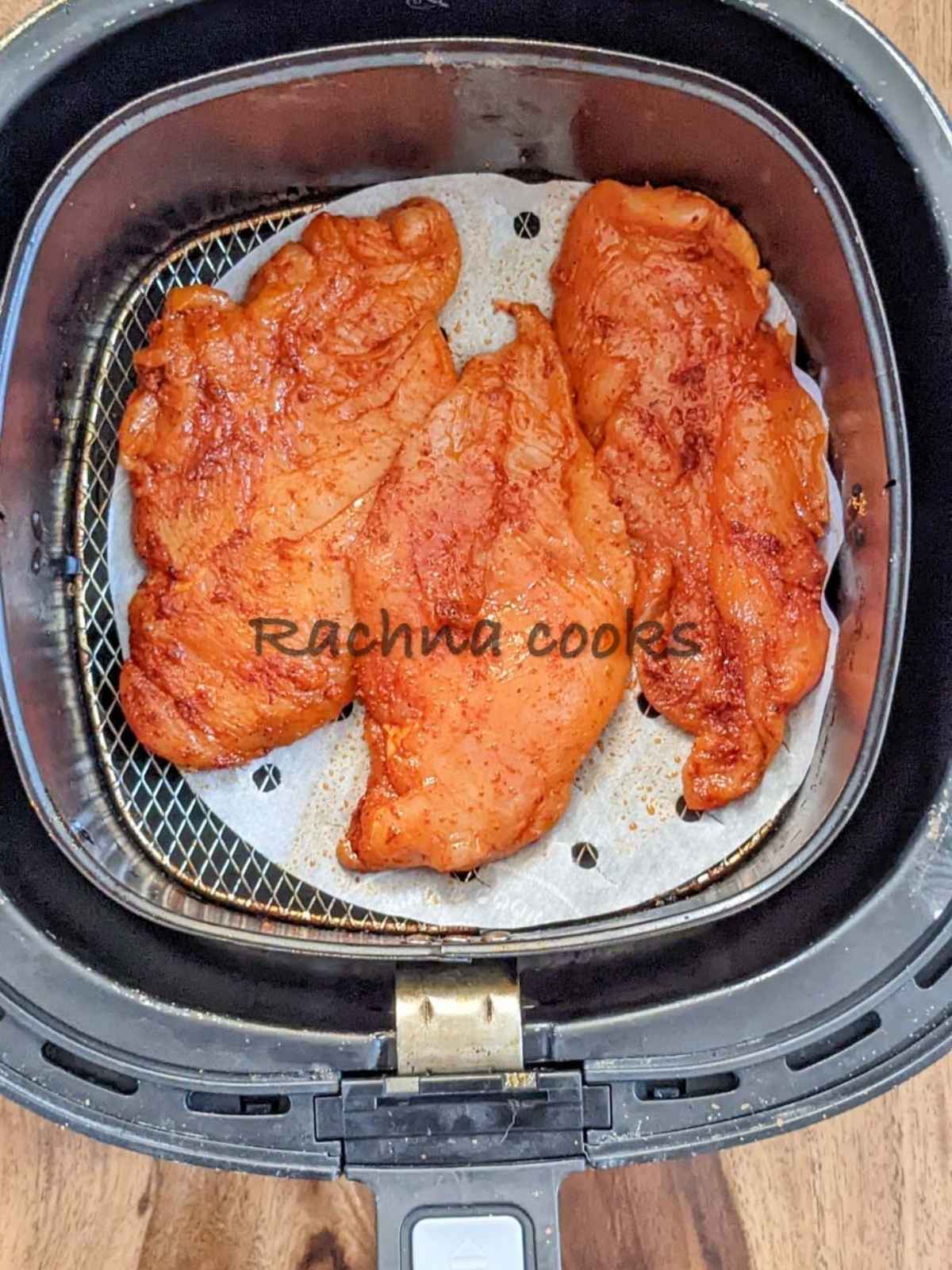 Chicken breasts with seasonings in air fryer basket.