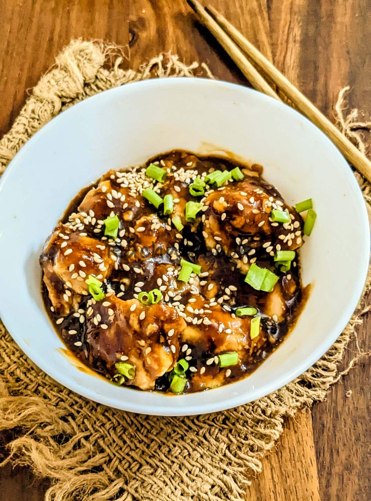 orange chicken garnished with scallions and sesame seeds and served in a bowl.