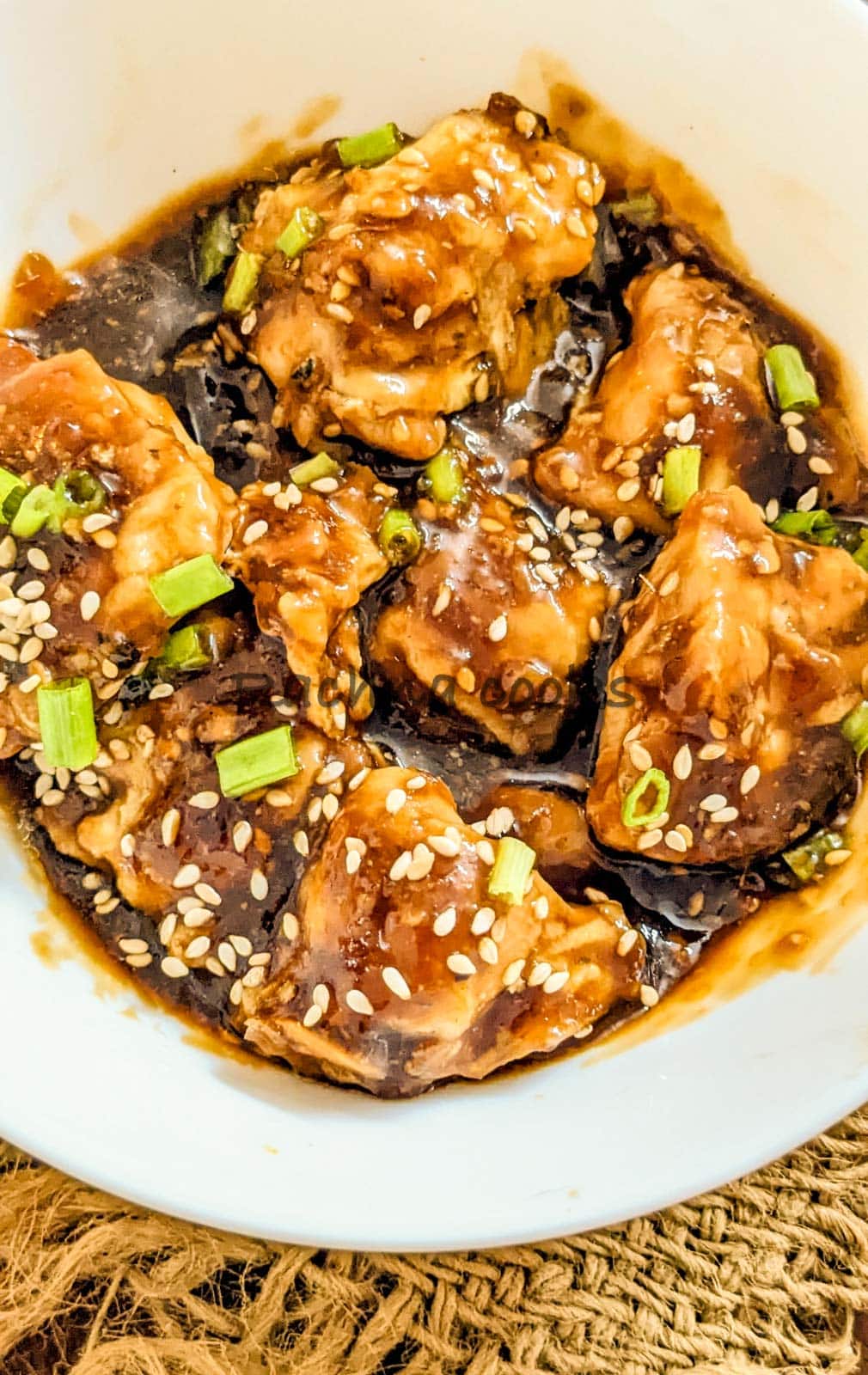 Close up of a bowlful of orange chicken garnished with scallions and sesame seeds.