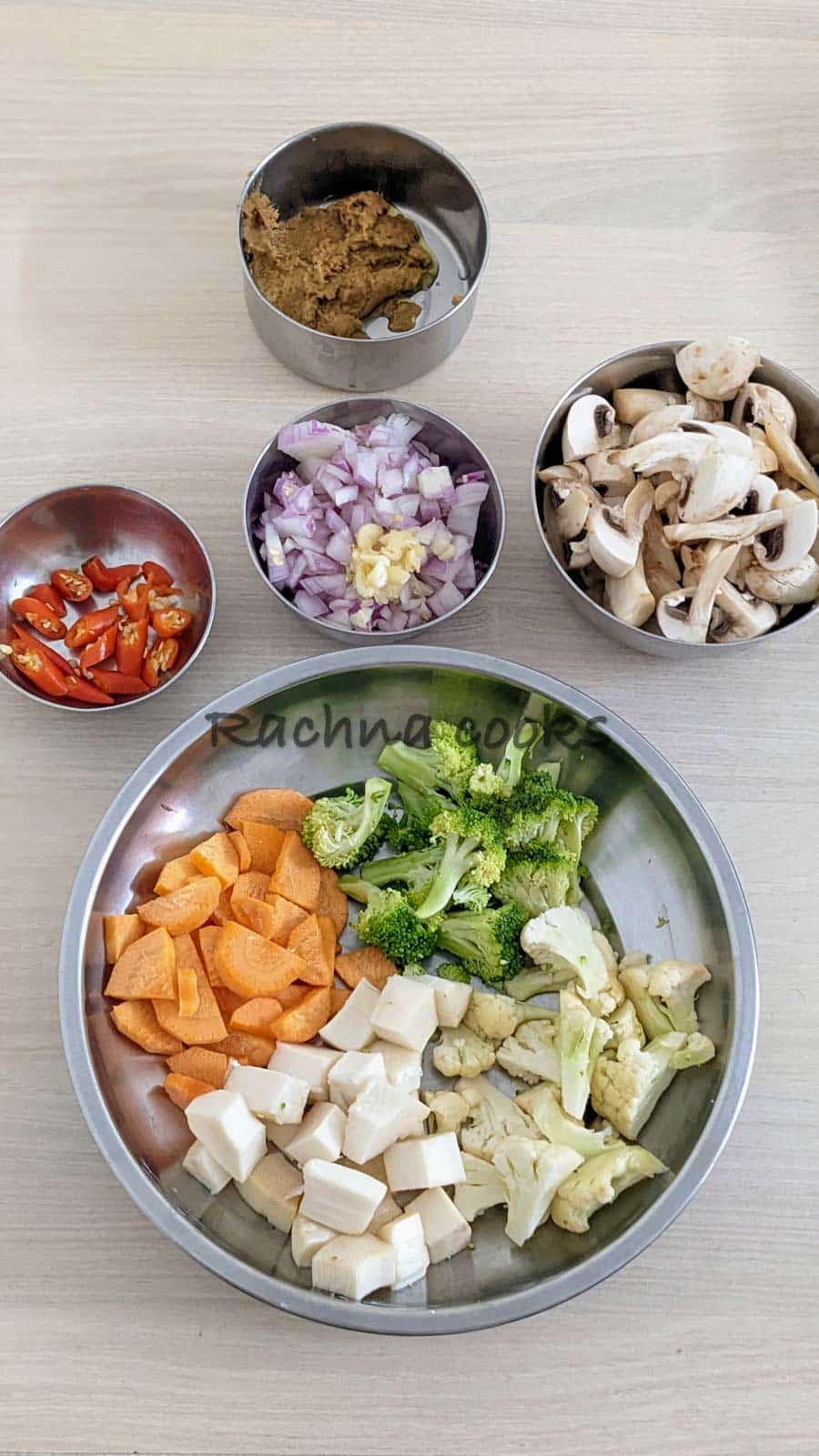 Bowls of chopped vegetables, mushrooms, onion, garlic, red chillies and tom kha paste.