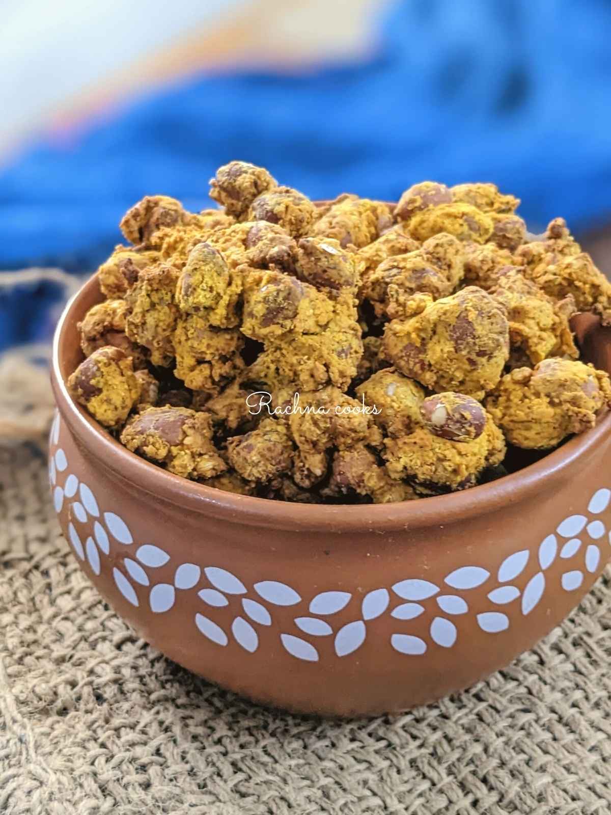 Masala peanuts in a brown ceramic bowl on a brown blue background.