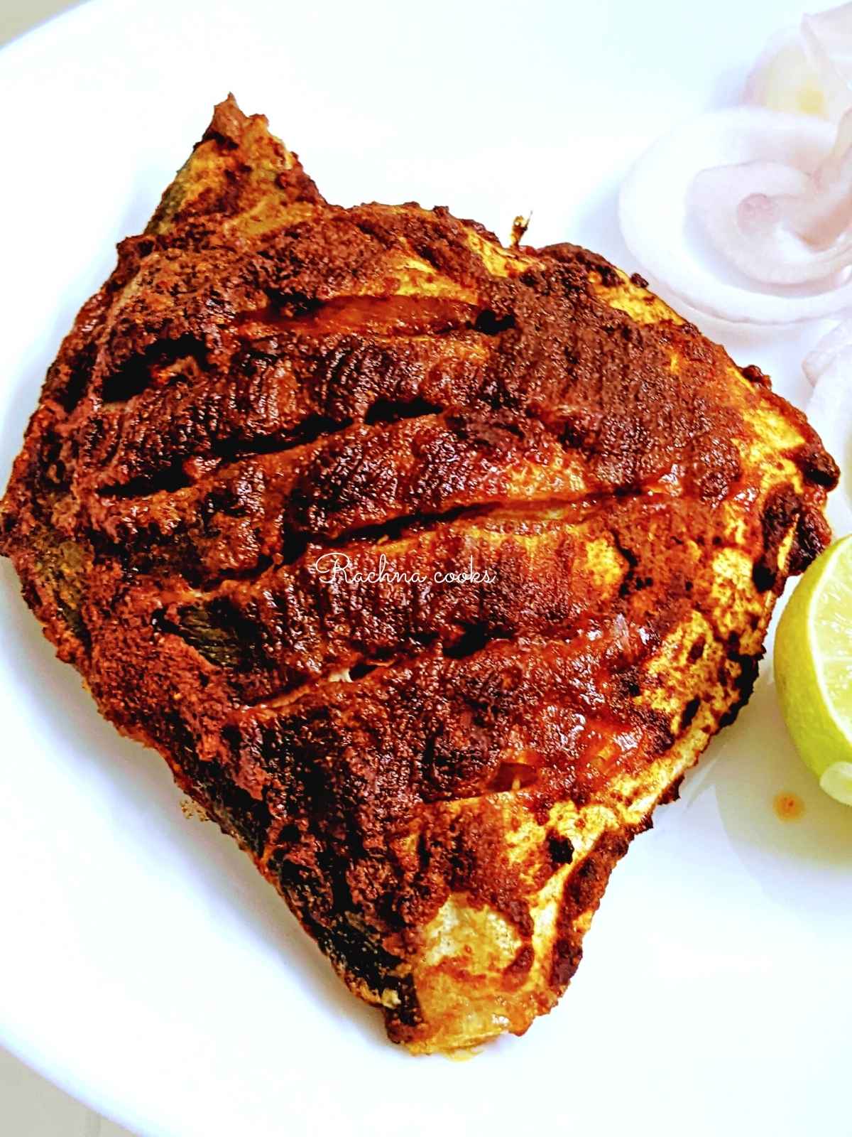 Top shot of Pomfret fry in a red masala served on a white plate with lime and onion slices.