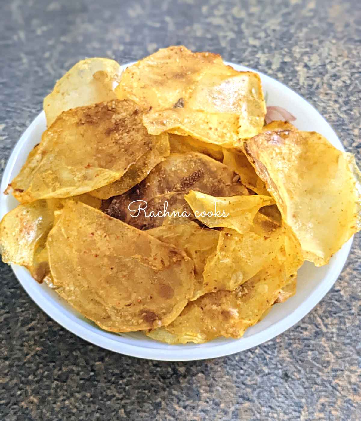 A bowl of crunchy potato chips against a grey background.