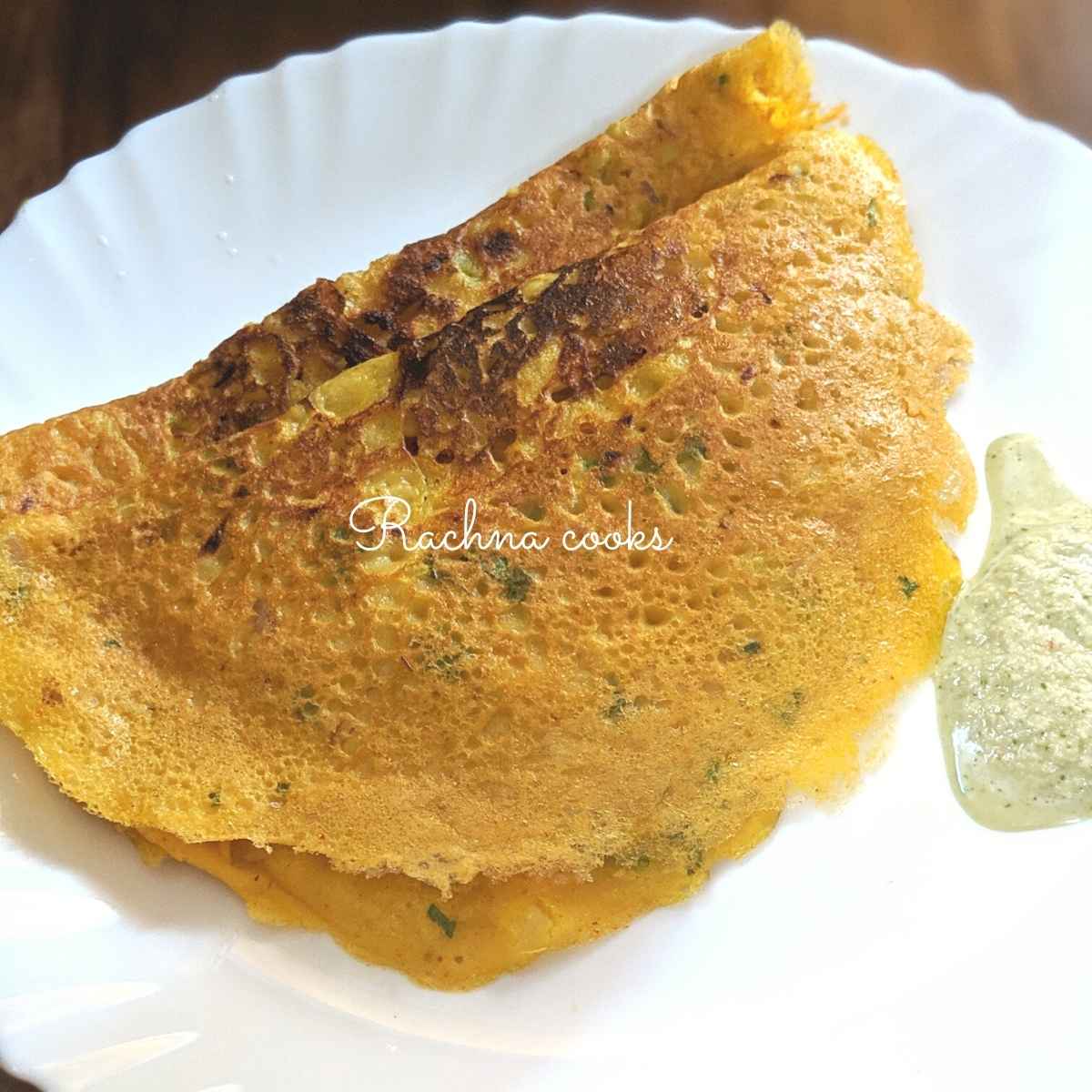 Two besan chillas or crepes on a white plate with chutney.