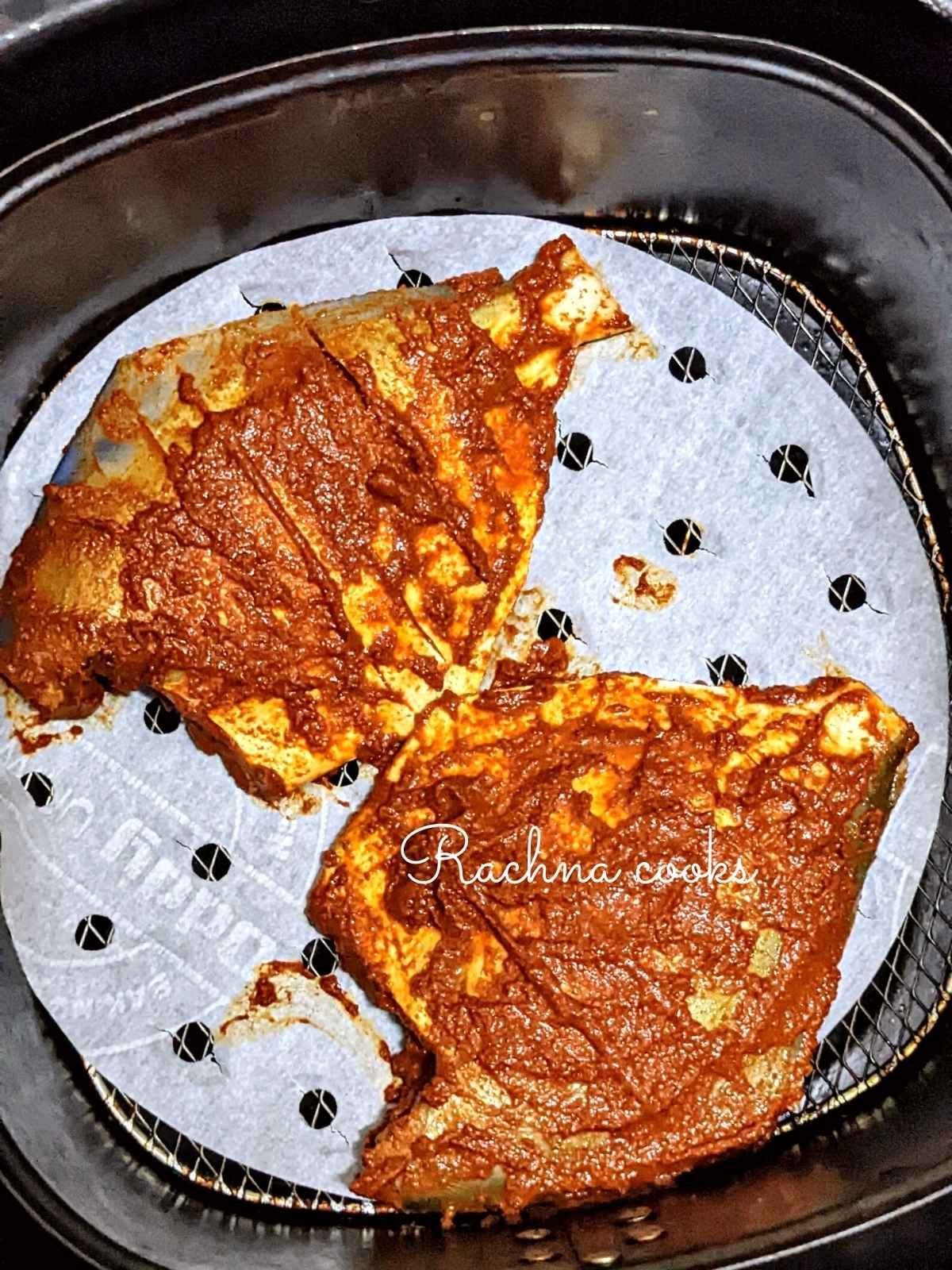 2 pomfret fish coated with masala and placed in air fryer basket for frying.