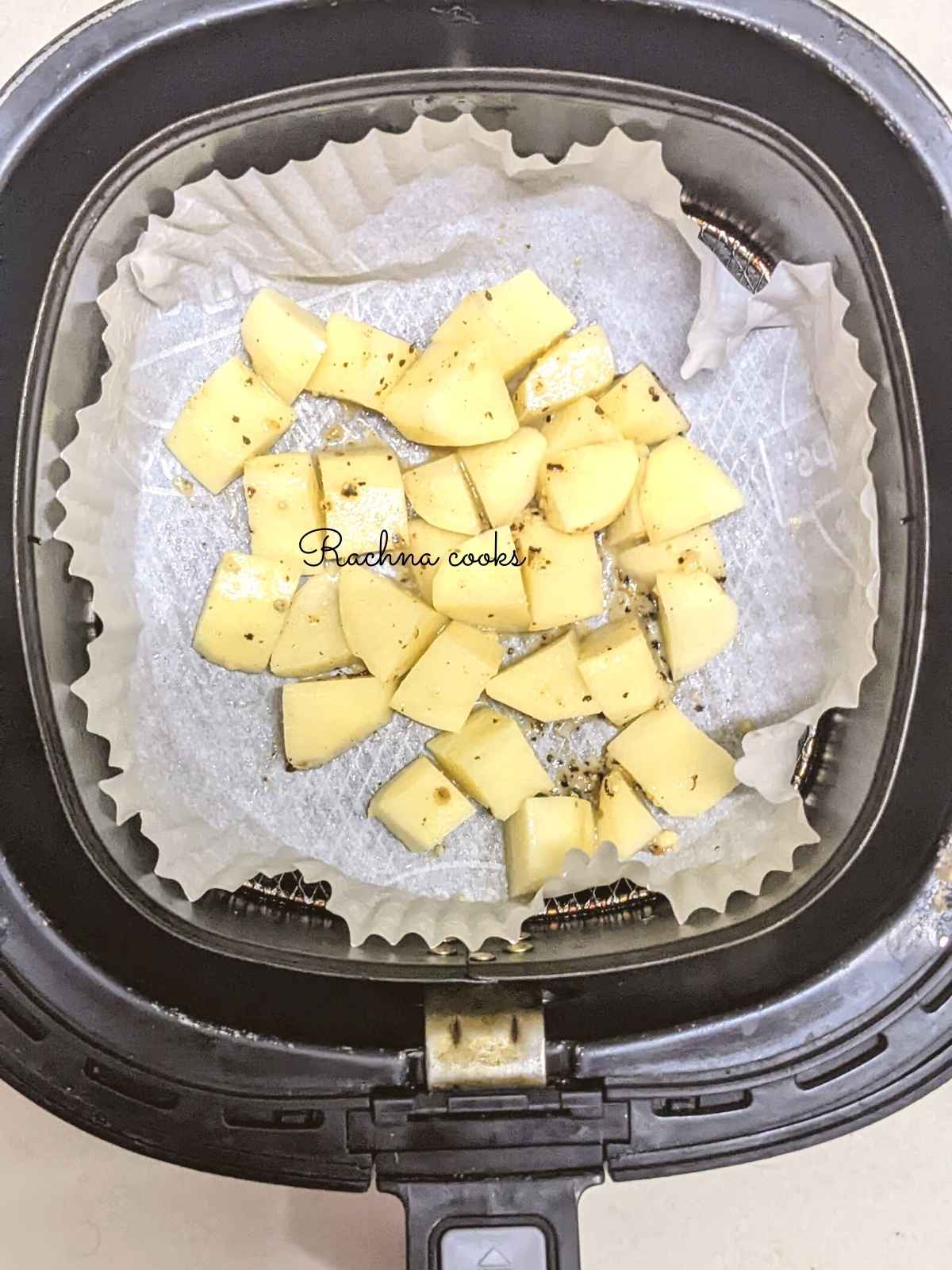 Potato cubes on a parchment paper dish in air fryer basket.