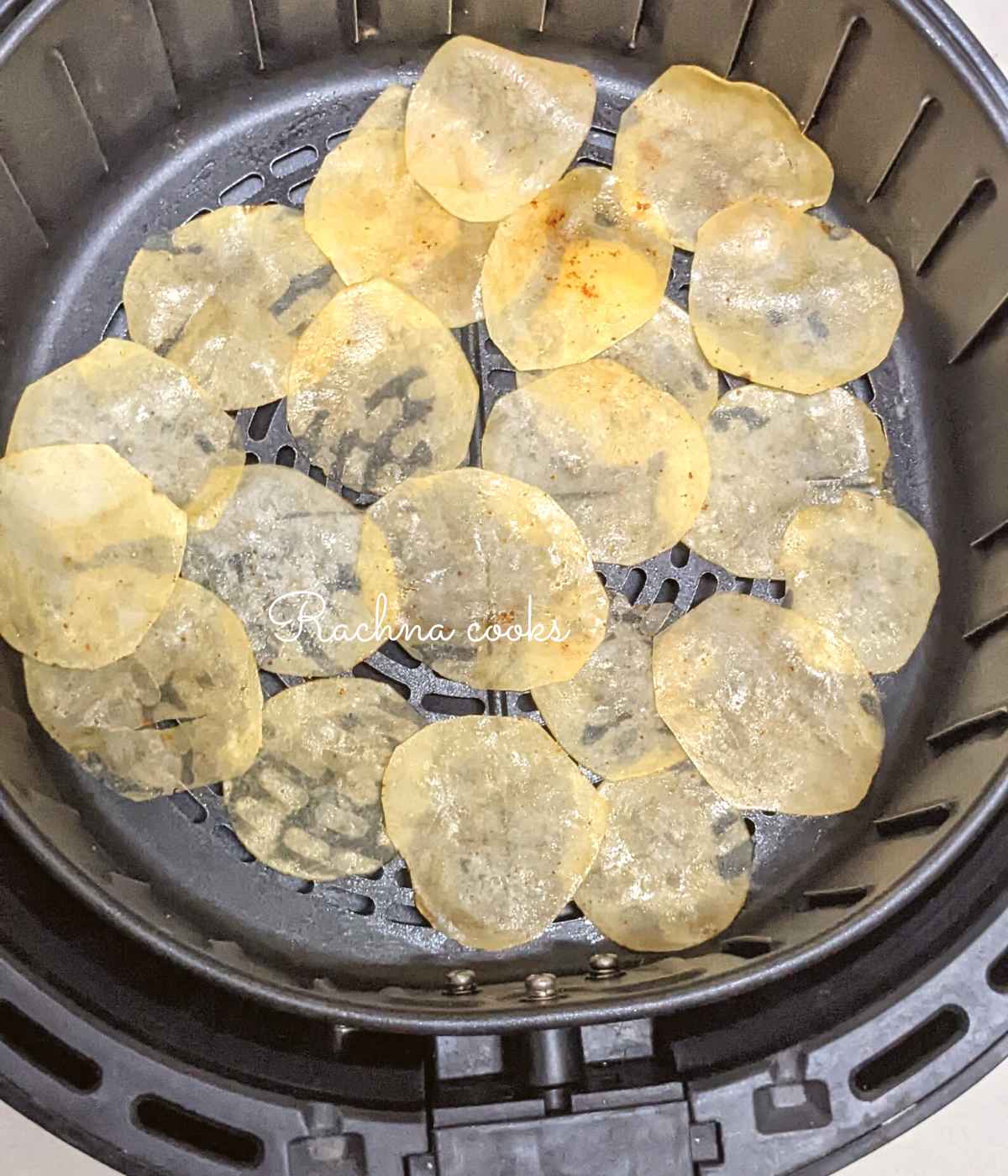 Seasoned potato slices spread out in air fryer basket ready for air frying.
