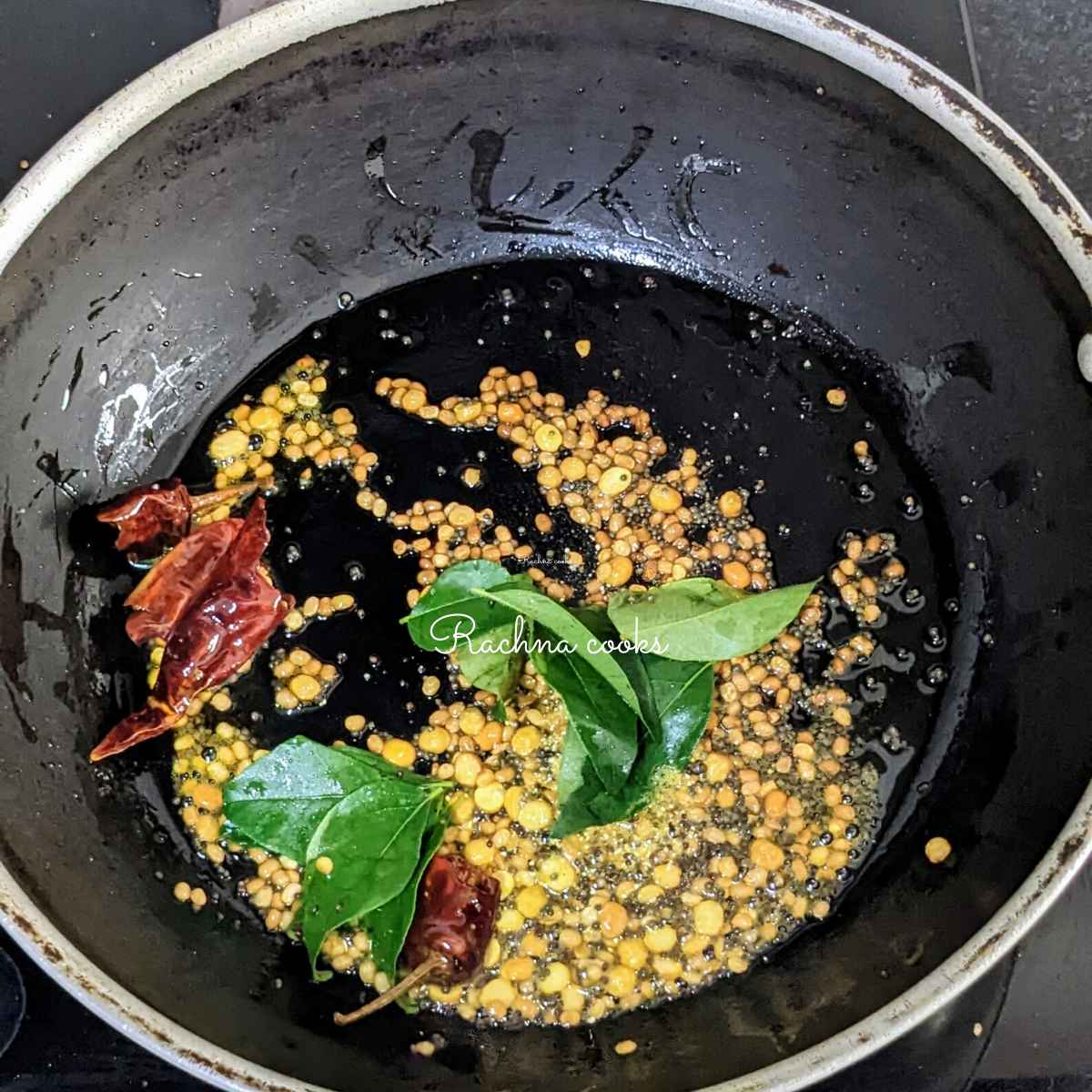 Toasted lentils, mustard seeds, broken red chillies and curry leaves in oil in a wok