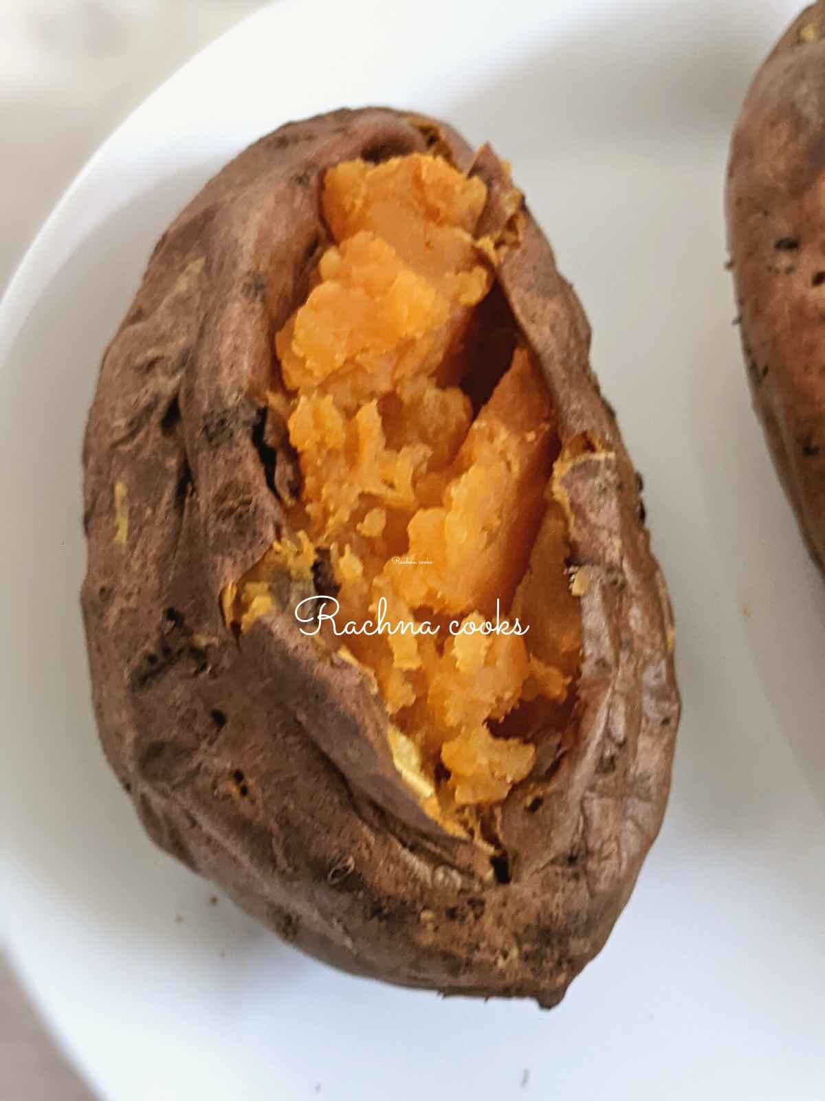 One large air fried baked sweet potato with wrinkly skin and fluffy flesh on a white plate.