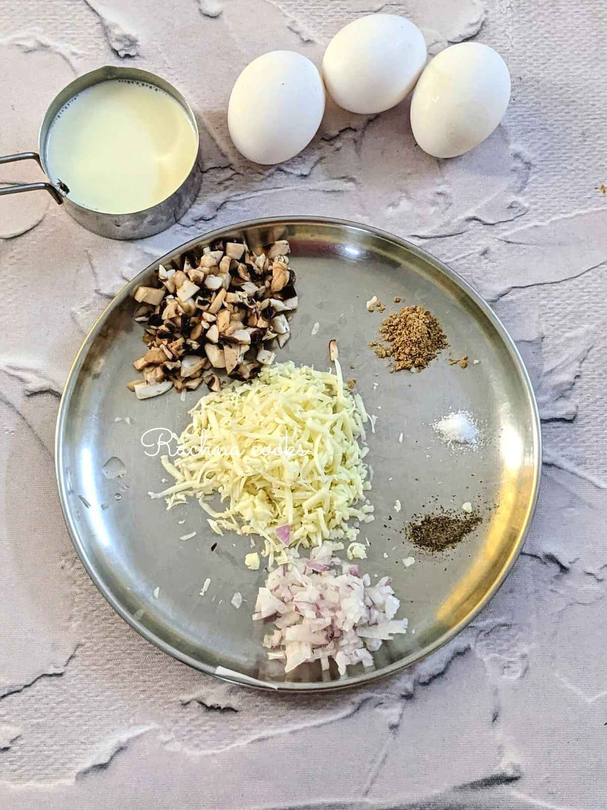 Ingredients for making egg bites: whole eggs, milk, cheese, garlic powder, salt, pepper, chopped mushroom and onion on a plate.