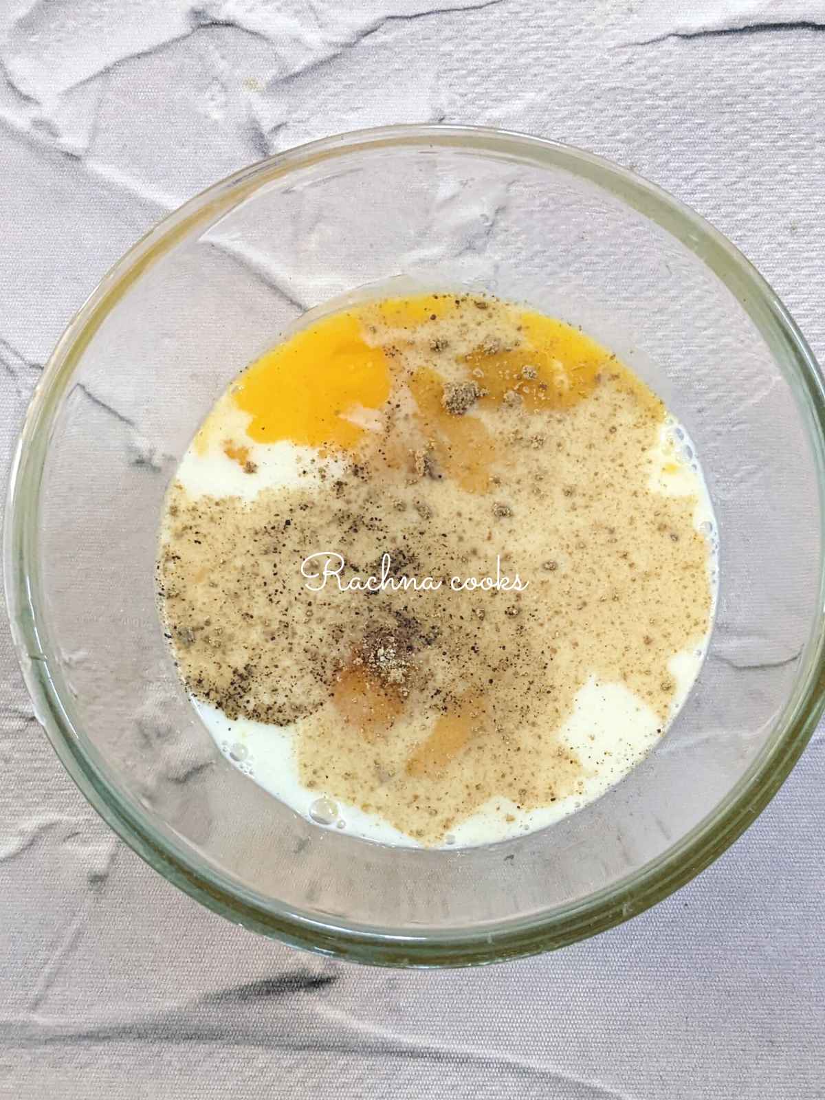 Eggs with milk, salt, pepper and garlic powder in a glass bowl.
