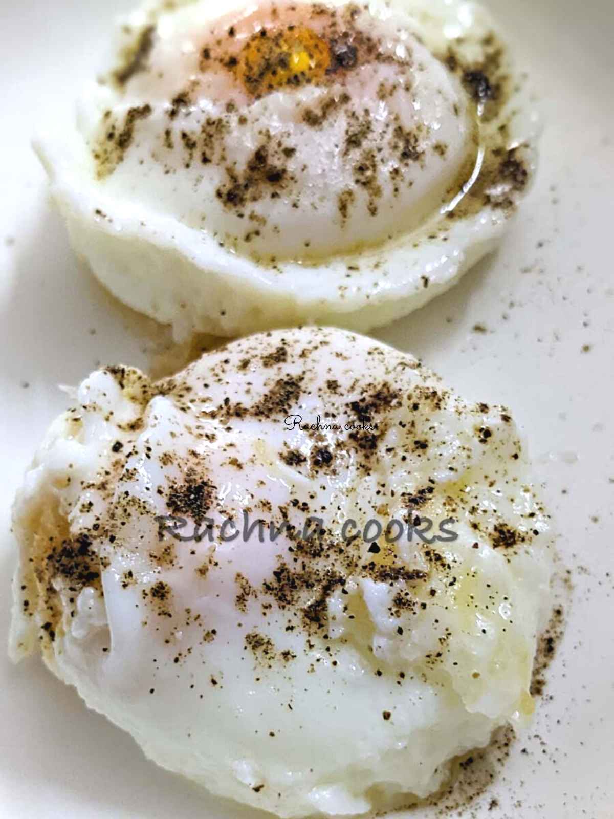 Close up of 2 poached eggs garnished with salt and pepper on a white plate.