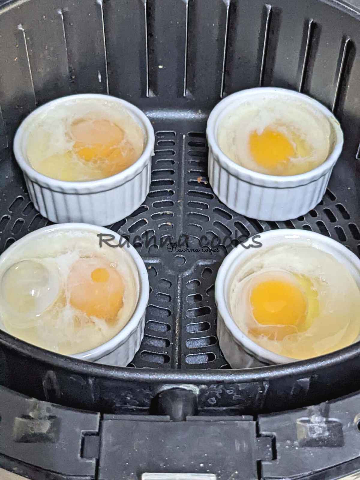 4 ramekins with broken eggs topped with hot water in them placed in air fryer basket.