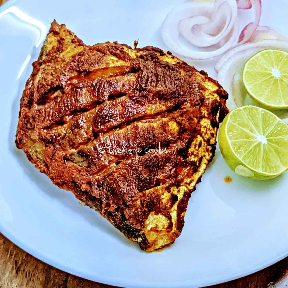 Pomfret fry in a red masala served on a white plate with lime and onion slices.