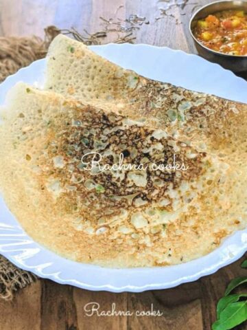 Two rava dosas stacked on top of each other served on a white plate.