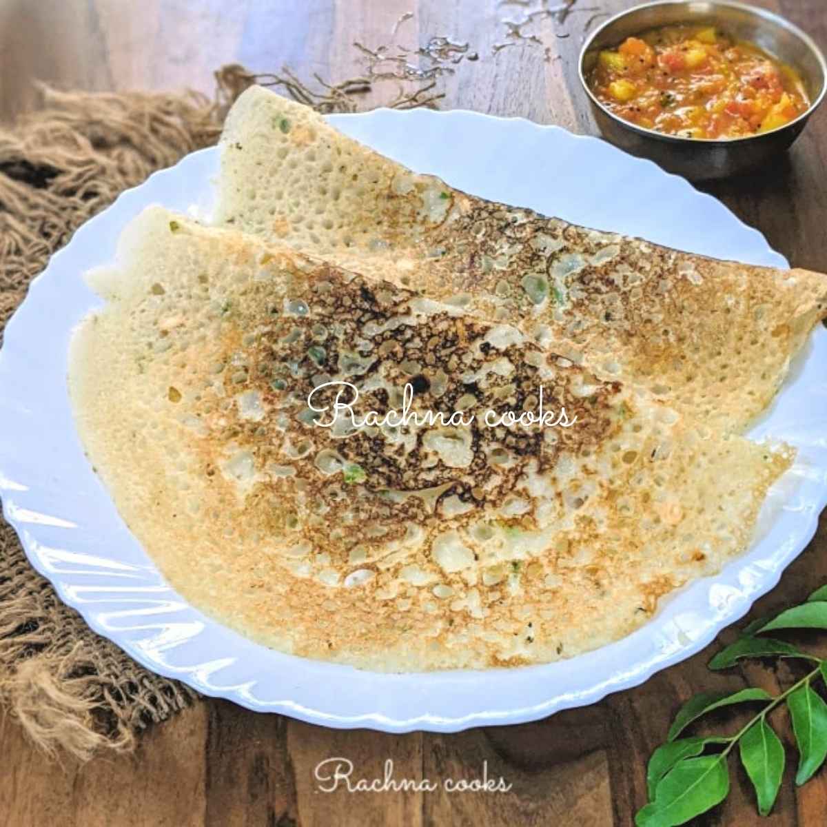 Two rava dosas folded and served in a white plate with tomato chutney in the background.