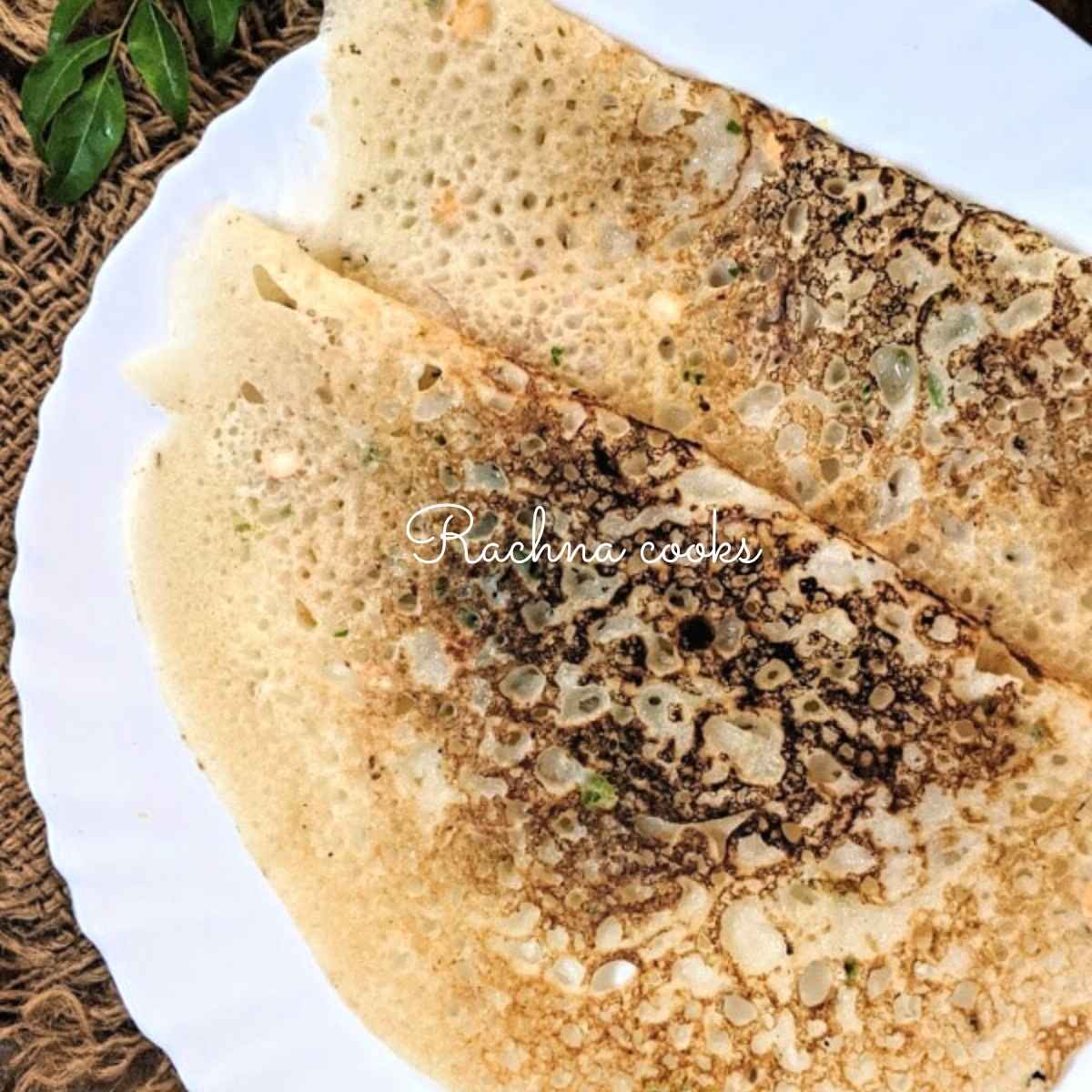 Top shot of two rava dosas on top of each other on a white plate.