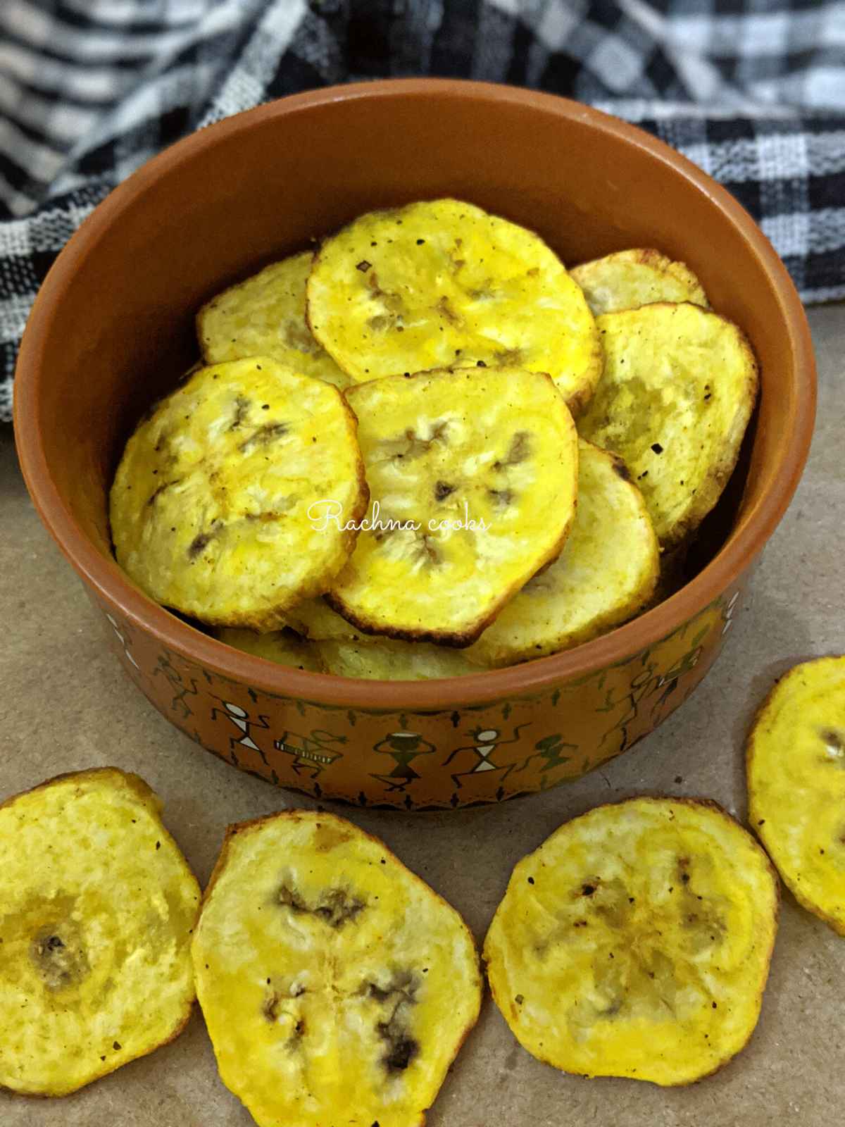 Golden plantain chips after air frying in a brown bowl. A few are also strewn down.