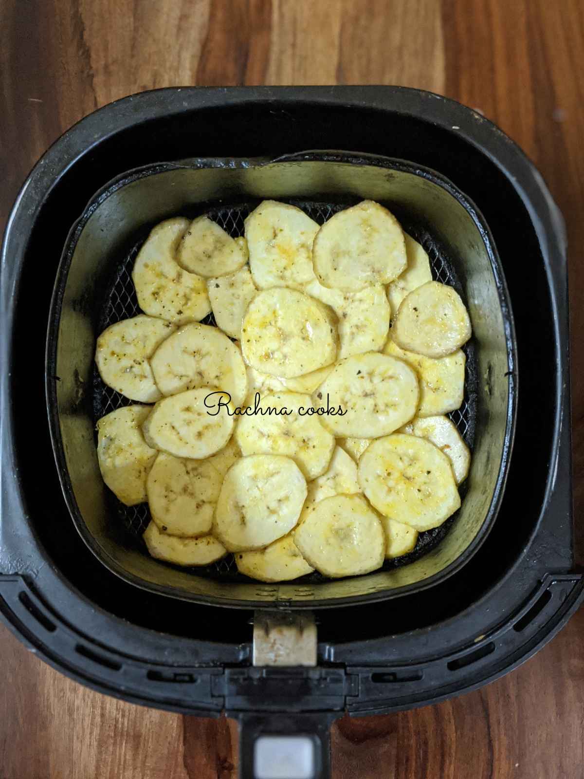 Banana chips tossed with seasoning and oil placed in air fryer basket.