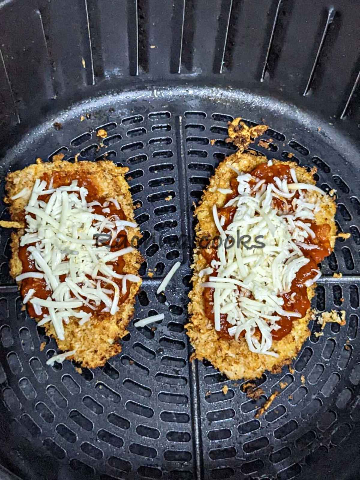 Breaded chicken fillet topped with marinara sauce and cheese in air fryer basket.