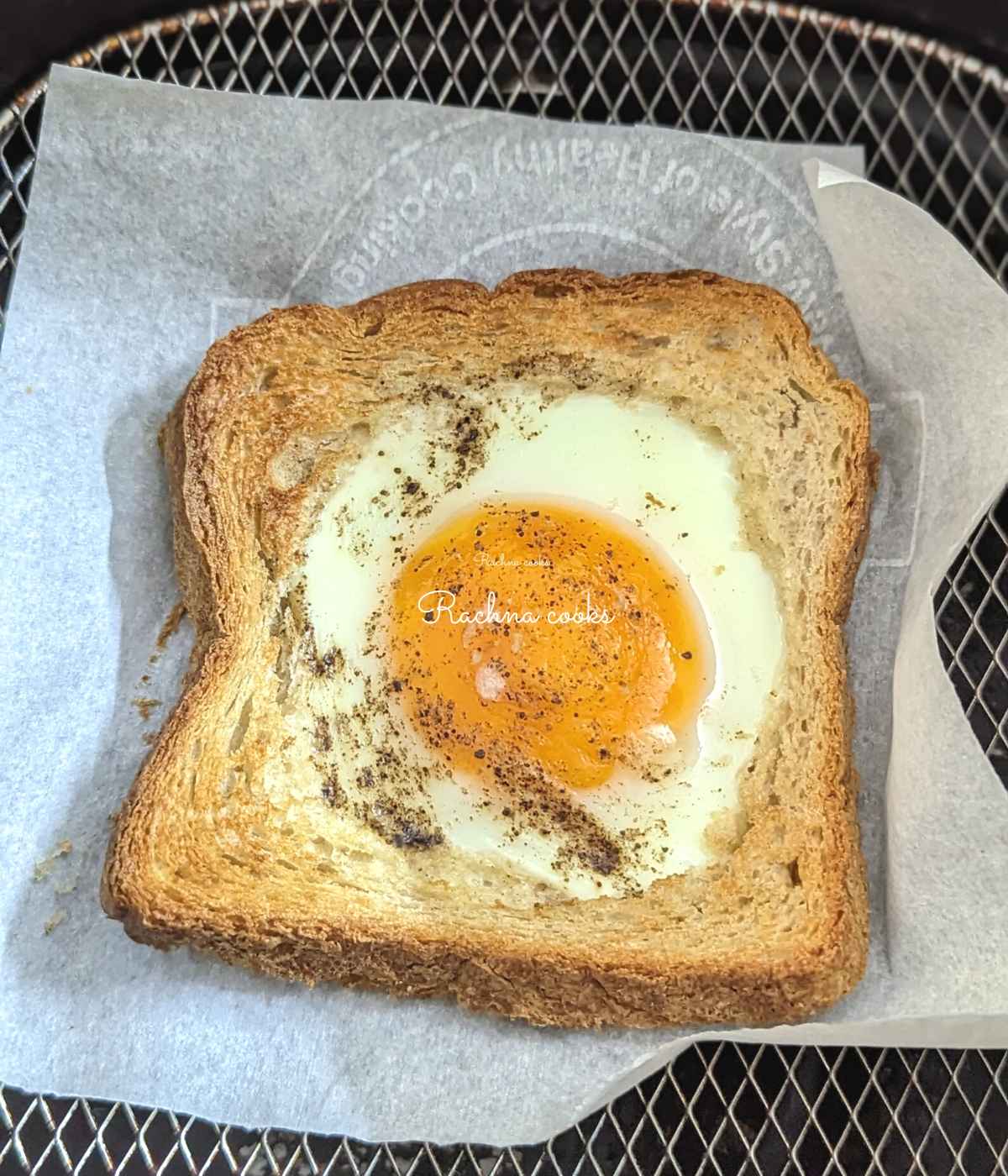 Egg toast on parchment paper in air fryer basket.