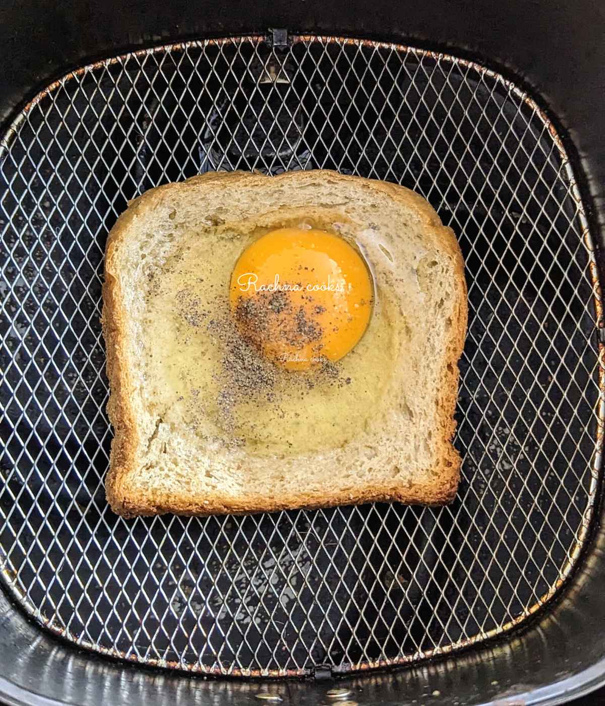 One slice of bread with a broken egg, salt and pepper on air fryer basket
