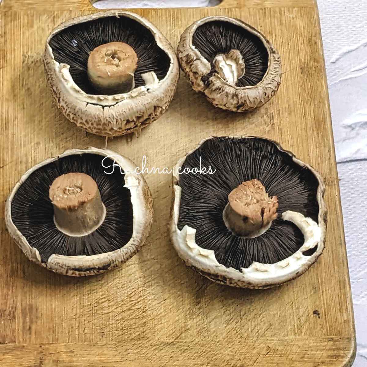 4 cleaned portobello mushrooms stalk side up on a chopping board.