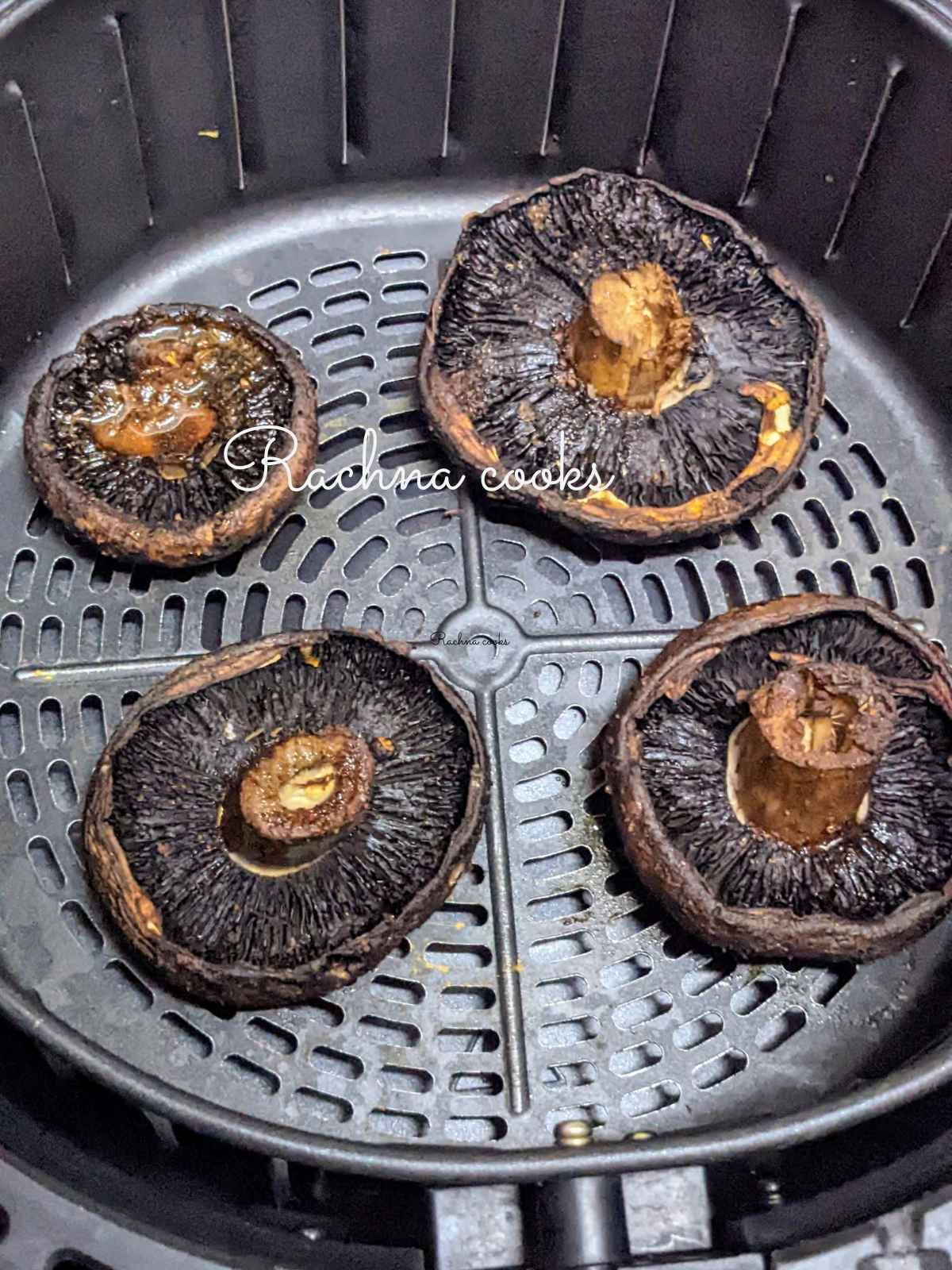 Four air fried portobello mushrooms in air fryer basket.
