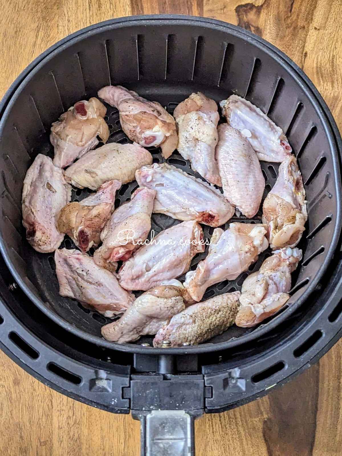 Chicken wings rubbed with salt and pepper in air fryer basket.