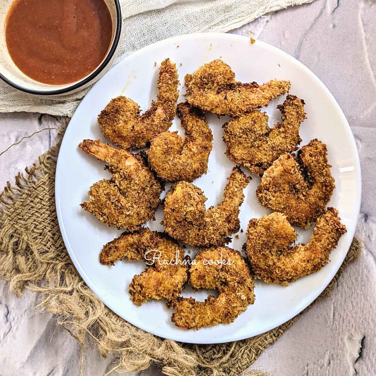 Crunchy air fried popcorn shrimp served on a white plate with a bowl of dip in the background