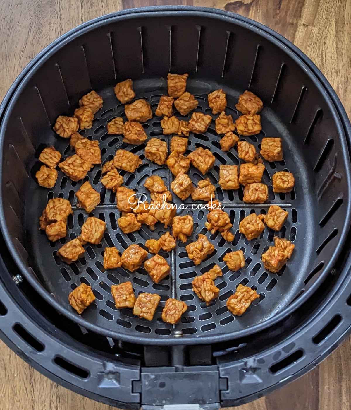 Marinated tempeh cubes laid out in air fryer basket ready for air frying.