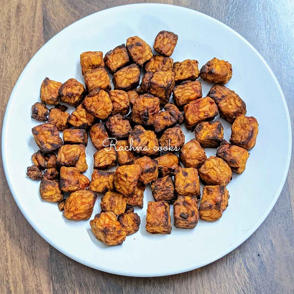 Air fried tempeh cubes on a white plate.