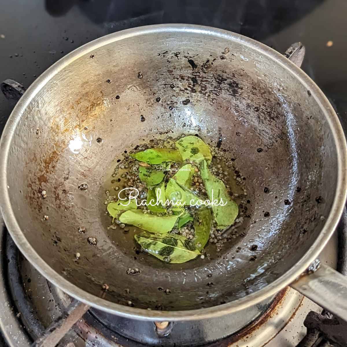 Tempering of curry leaves and mustard seeds in oil in a pan.