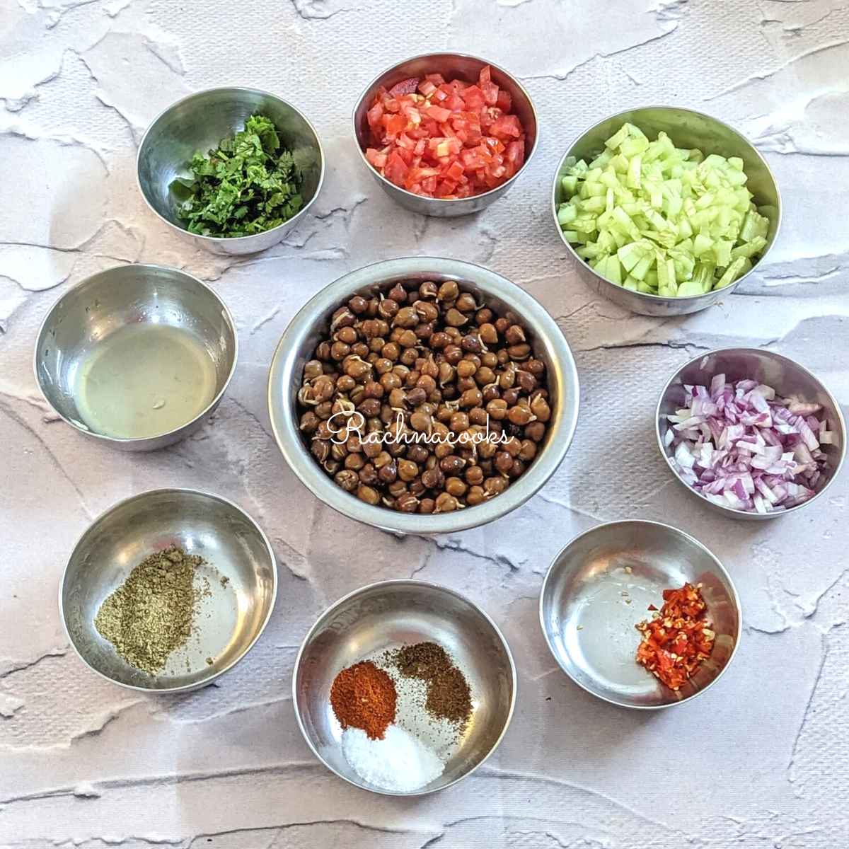 Ingredients for the salad are in bowls: boiled black chickpeas, chopped onion, cucumber, tomatoes, cilantro, chillies, lemon juice and spices.